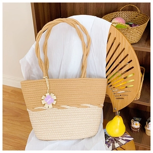 Détail d'un sac cabas bicolore en paille avec anses en corde et breloque fleur mauve