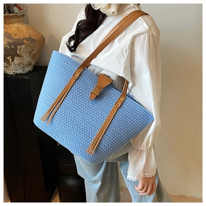 Dettaglio di una borsa tote blu intrecciata con spalline in pelle e decorazione con nappe