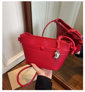 Détail du sac bandoulière rouge en cuir grainé avec sangle nouée et pendentif cœur