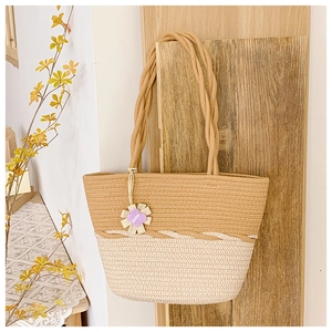 Détail d'un sac cabas bicolore en paille tressée avec anses et pendentif fleur décoratif