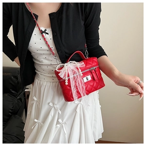 Détail du sac rouge matelassé avec nœud en dentelle et pendentif en perles
