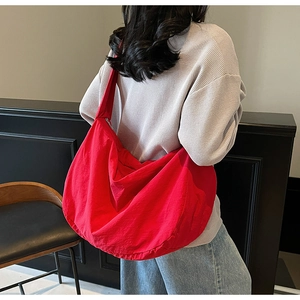 Gros plan d'un grand sac bandoulière en nylon rouge porté sur un pull gris chiné