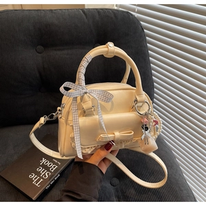 Detail of cream bowling bag featuring delicate lace trim, bow, and pearl chain strap