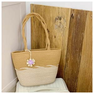 Detail of woven straw tote bag featuring two-tone color block and purple flower charm