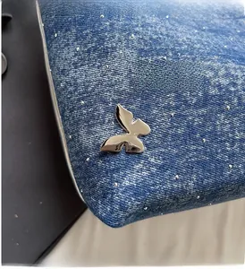 Detailed close-up of metallic silver butterfly buckle and studs on navy denim bag