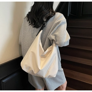 Detail view of large cream nylon tote bag with black leather strap on a model