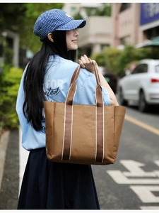 Outdoor street style view of a brown canvas tote bag with contrast shoulder straps