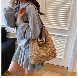 Detail of the woven straw texture and adjustable brown leather strap on the large hobo bag