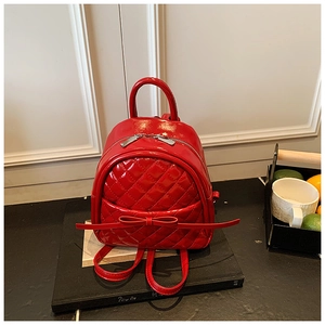 Vue détaillée de la texture matelassée du mini sac à dos rouge brillant avec nœud