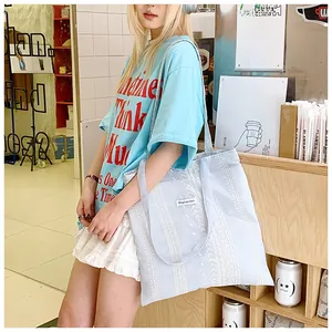 Detail view of light blue tote bag with white lace wave patterns and brand label