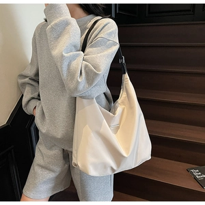 Close-up of a large beige crossbody tote bag with adjustable black strap on a model