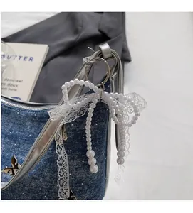Detail of beaded white pearl bow pendant with lace trim on a blue denim bag