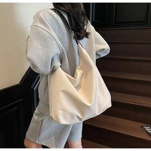 Detail of minimalist cream tote bag showing supple fabric and black leather shoulder strap