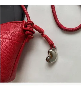 Détail du sac en cuir grainé rouge avec bandoulière tressée et pendentif argenté