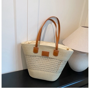 Dettaglio borsa tote in paglia con manici in pelle marrone e logo del marchio in stile vita
