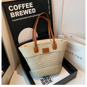 Dettaglio ravvicinato della borsa tote in paglia con manici in pelle marrone e logo