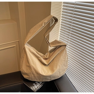 Détail du sac bandoulière minimaliste en nylon beige sur un canapé sombre élégant