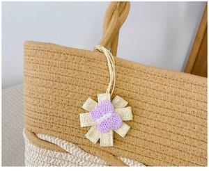 Close-up of handmade woven straw tote featuring a floral pendant and natural cotton texture