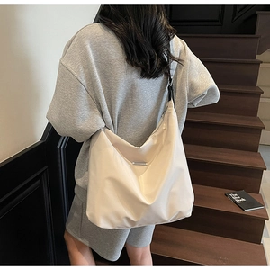 Detail of a creamy white oversized tote bag with metal tag and black textile strap