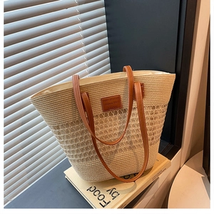 Dettaglio di borsa tote in paglia intrecciata con manici in pelle marrone e toppa