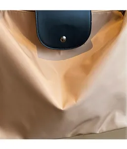 Detail of champagne nylon fabric with black leather flap and metallic rivet on tote bag