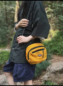 Dettaglio di una borsa a tracolla in nylon giallo brillante con cerniera nera e toppa