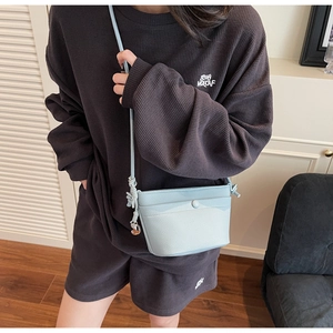 Détail d'un sac bandoulière bleu clair en cuir grainé avec bandoulière nouée et pendentif