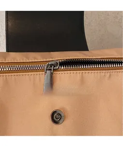 Detail of silver metal zipper puller and magnetic snap closure on khaki nylon tote bag