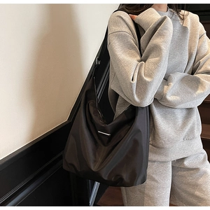 Detail of a large black half-moon shoulder bag with sleek nylon texture and metal buckle