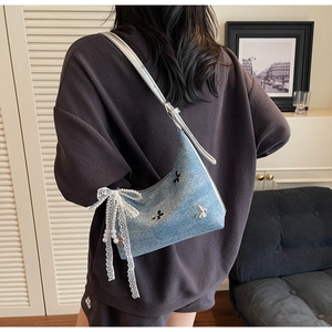 Detail of light blue denim shoulder bag with white lace bow and butterfly appliques