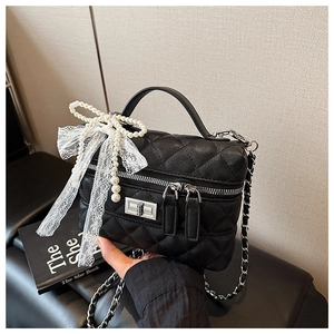 Détail du sac matelassé noir avec nœud en dentelle blanche, perle et fermoir argenté