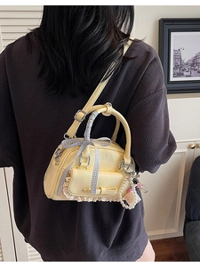 Pale yellow patent leather bowling bag with bow and pearl charms worn by model