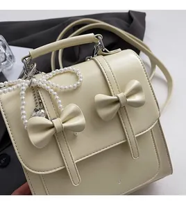 Détail d'un sac à dos blanc cassé élégant avec pendentif en perles et nœuds décoratifs