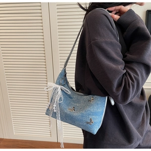Close-up of blue denim crescent bag featuring silver butterfly accents and pearl lace charm