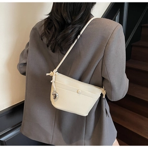 Détail du sac bandoulière en cuir crème avec bandoulière tressée et pendentif cœur