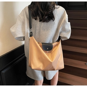Detail of a large beige nylon tote bag with black leather flap worn by a model