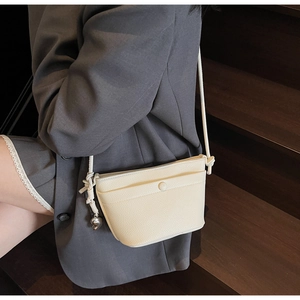 Détail du sac bandoulière en cuir blanc crème avec sangle nouée et breloque coeur en argent
