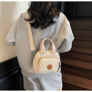 Detailansicht der beigen Nylon-Umhängetasche mit Logo-Patch und verstellbarem Gurt