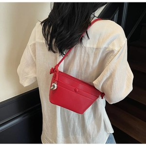 Détail du sac bandoulière en cuir rouge grainé avec bandoulière nouée et breloque cœur argenté