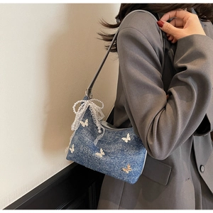 Detail of blue denim shoulder bag with white butterfly appliques and lace pearl charm