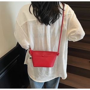 Détail d'un sac seau en cuir rouge avec texture litchi et pendentif boule métallique