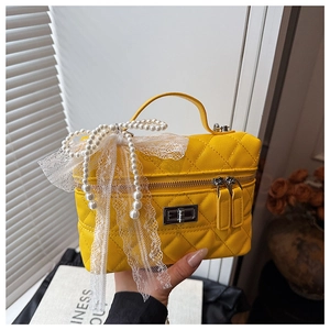 Détail du sac matelassé jaune avec un nœud en dentelle et des pendentifs en perles