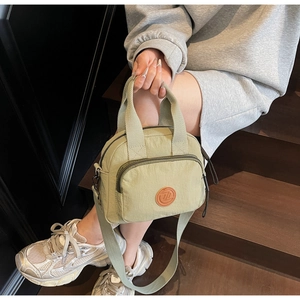 Detailansicht einer olivgrünen Nylon-Handtasche mit rundem Logo und verstellbarem Riemen