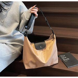 Detail of a large khaki nylon hobo bag with black leather straps on wooden stairs