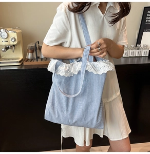 Detail of blue striped canvas tote bag featuring delicate white lace trim and shoulder strap