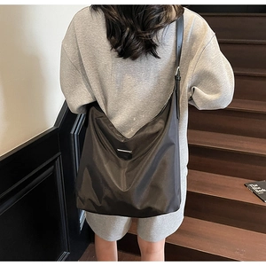 Model wearing a large black minimalist nylon crossbody tote bag on modern wood stairs