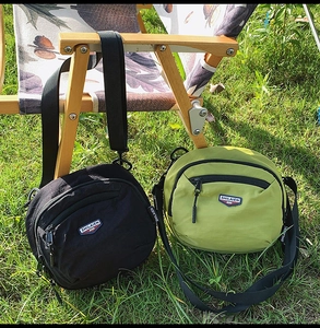 Dettaglio di borse a tracolla in nylon nero e verde oliva su una sedia di legno all'aperto
