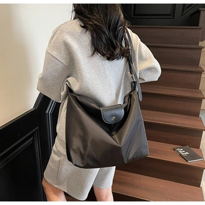 Detail of black nylon tote bag featuring leather flap, silver metal snap and adjustable strap