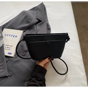 Vue de dessus d'un sac seau en cuir grainé noir avec blazer gris et livre décoratif