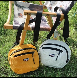 Dettaglio di borse a tracolla in nylon giallo e beige con logo su una sedia pieghevole